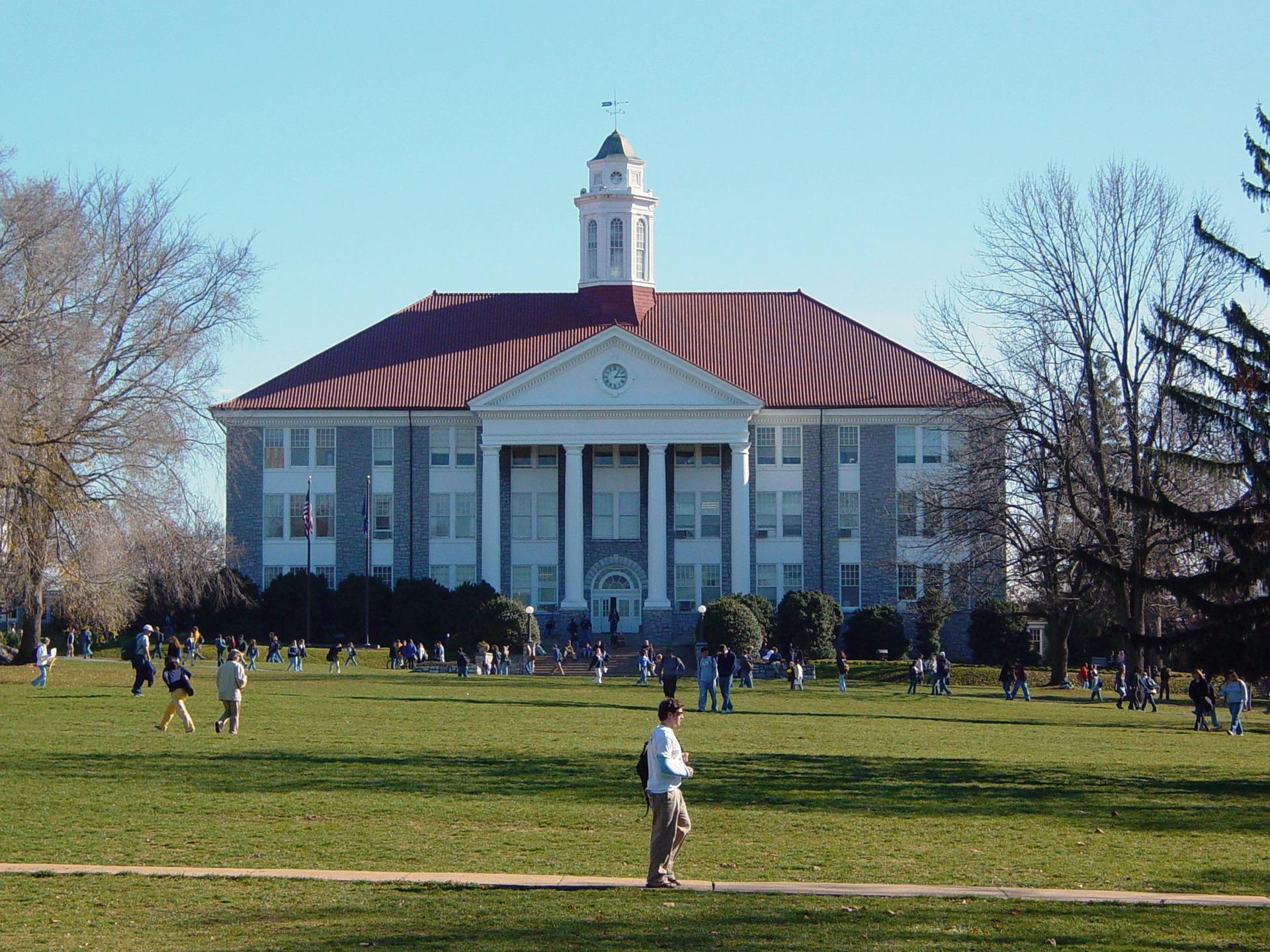 Large building with clock tower, people on sunny green lawn.