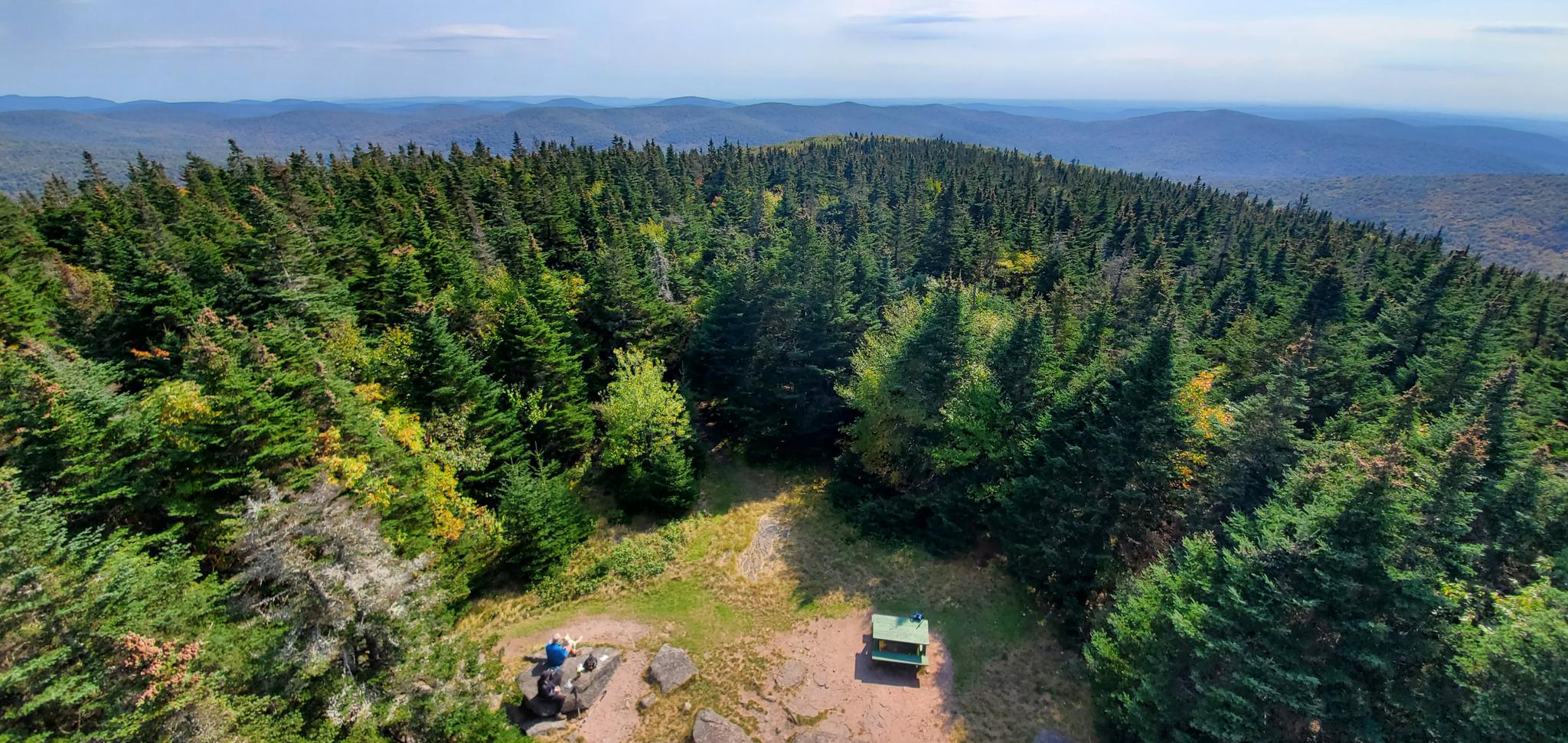 Overhead view of a forested mountain peak with a small clearing and picnic table.