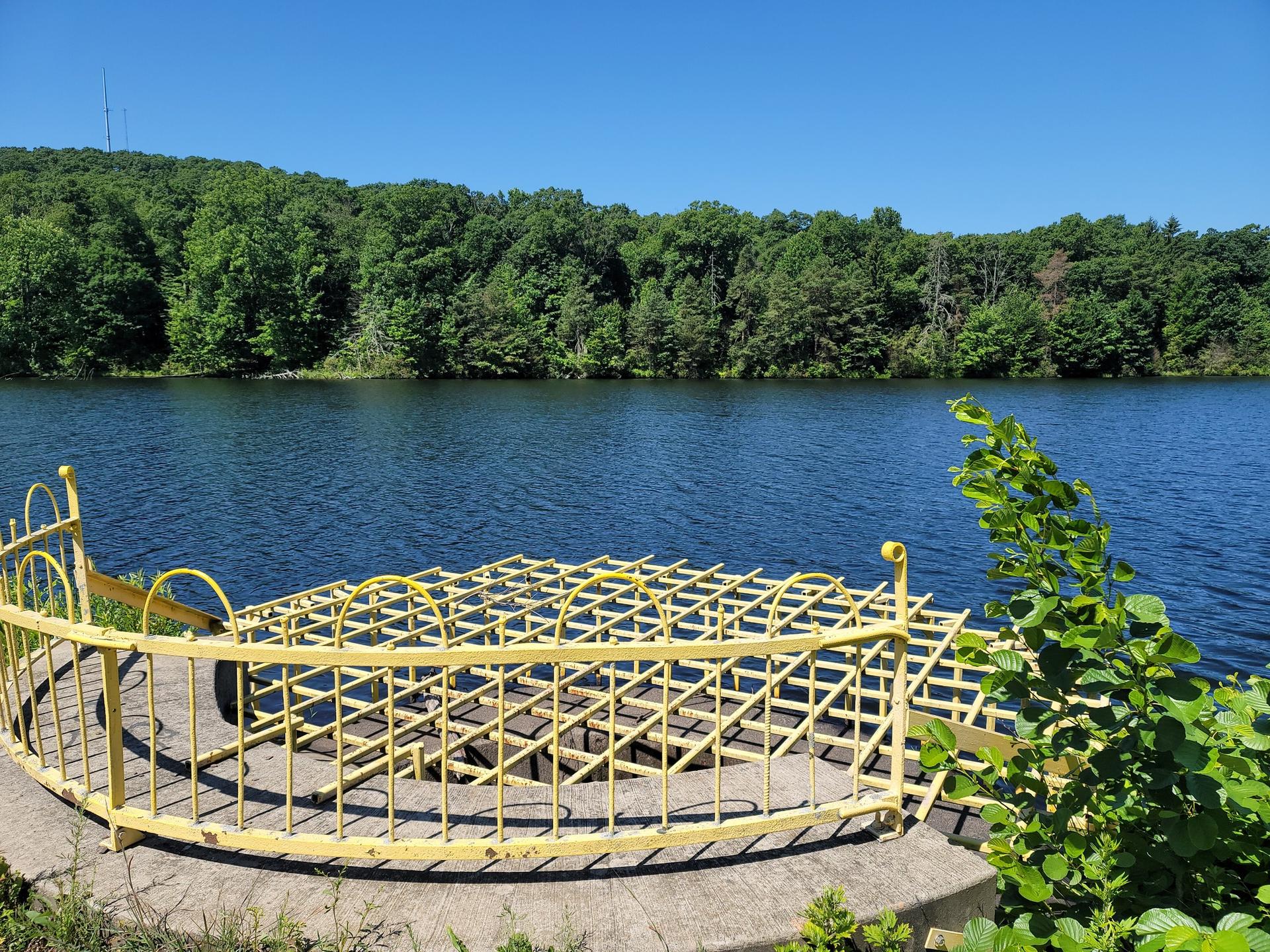 Bright yellow metal structure on a concrete platform by a calm lake.