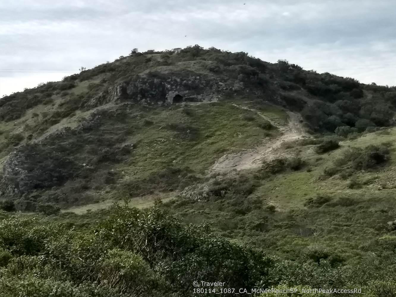Grassy hill with a small cave entrance and a faint dirt path.