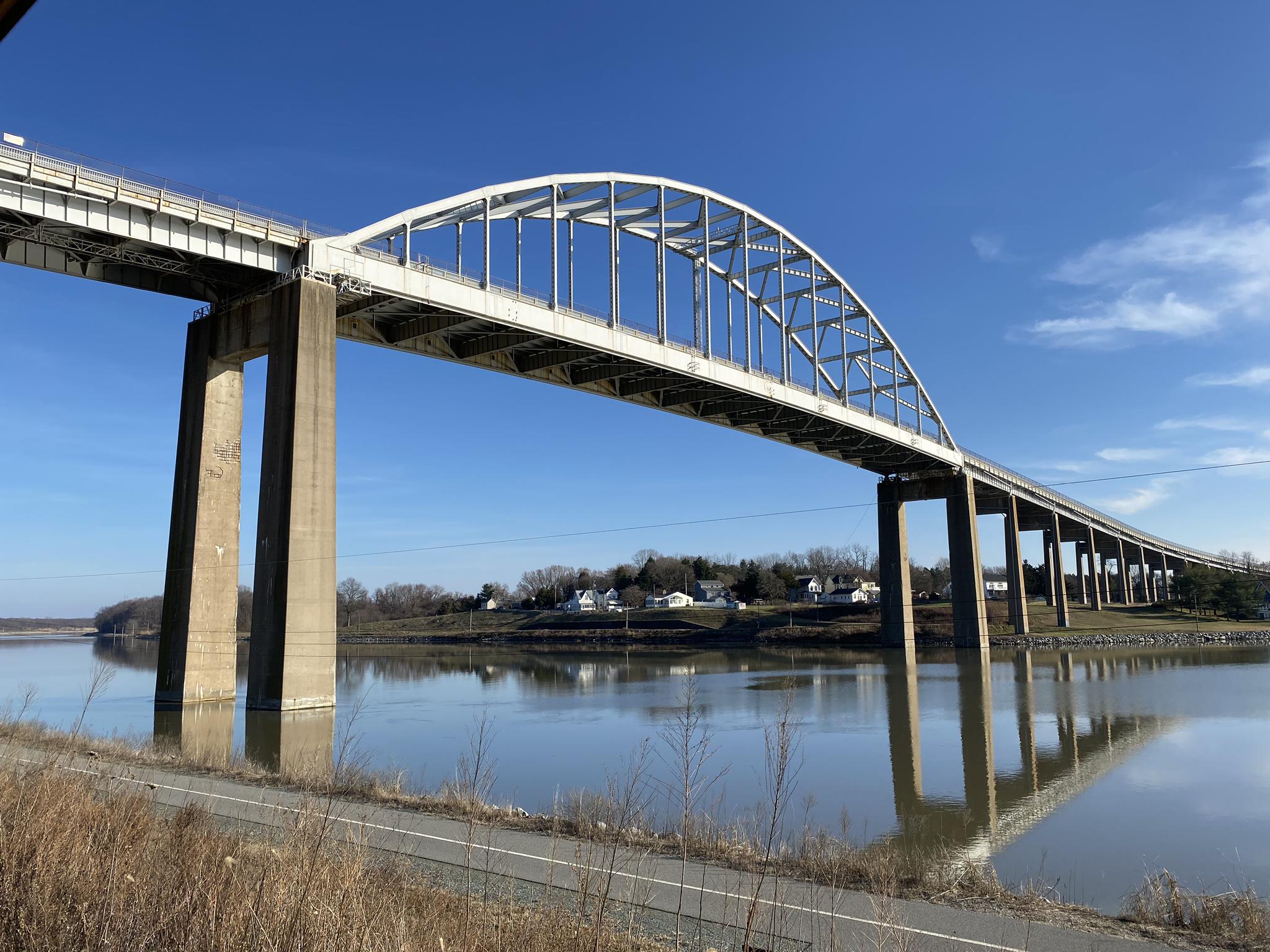 A large arched bridge spans a calm river with reflections under blue sky.