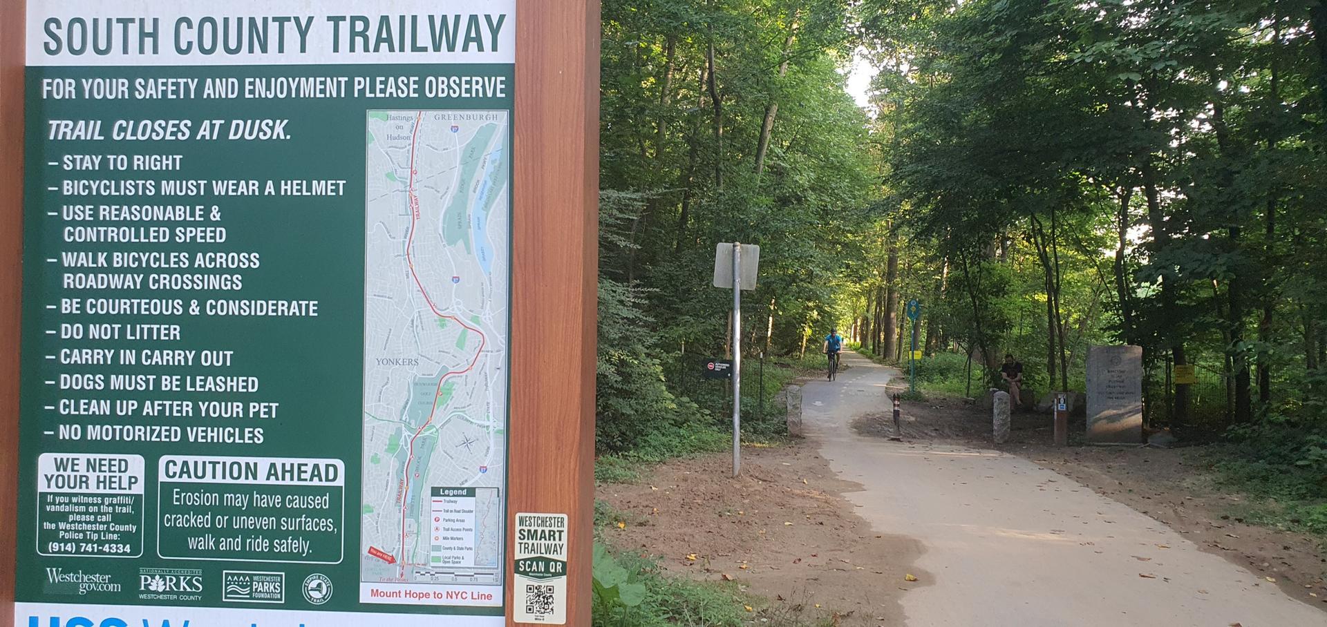 Green trail rules sign next to a dirt path entering a dense forest.