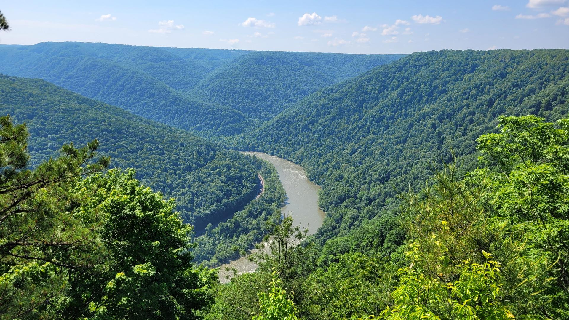 A winding river cuts through a lush green valley under a clear sky.