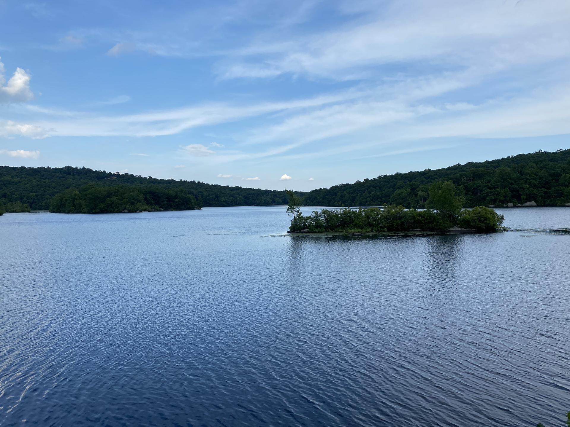 Blue lake with a small tree-covered island under a partly cloudy sky.