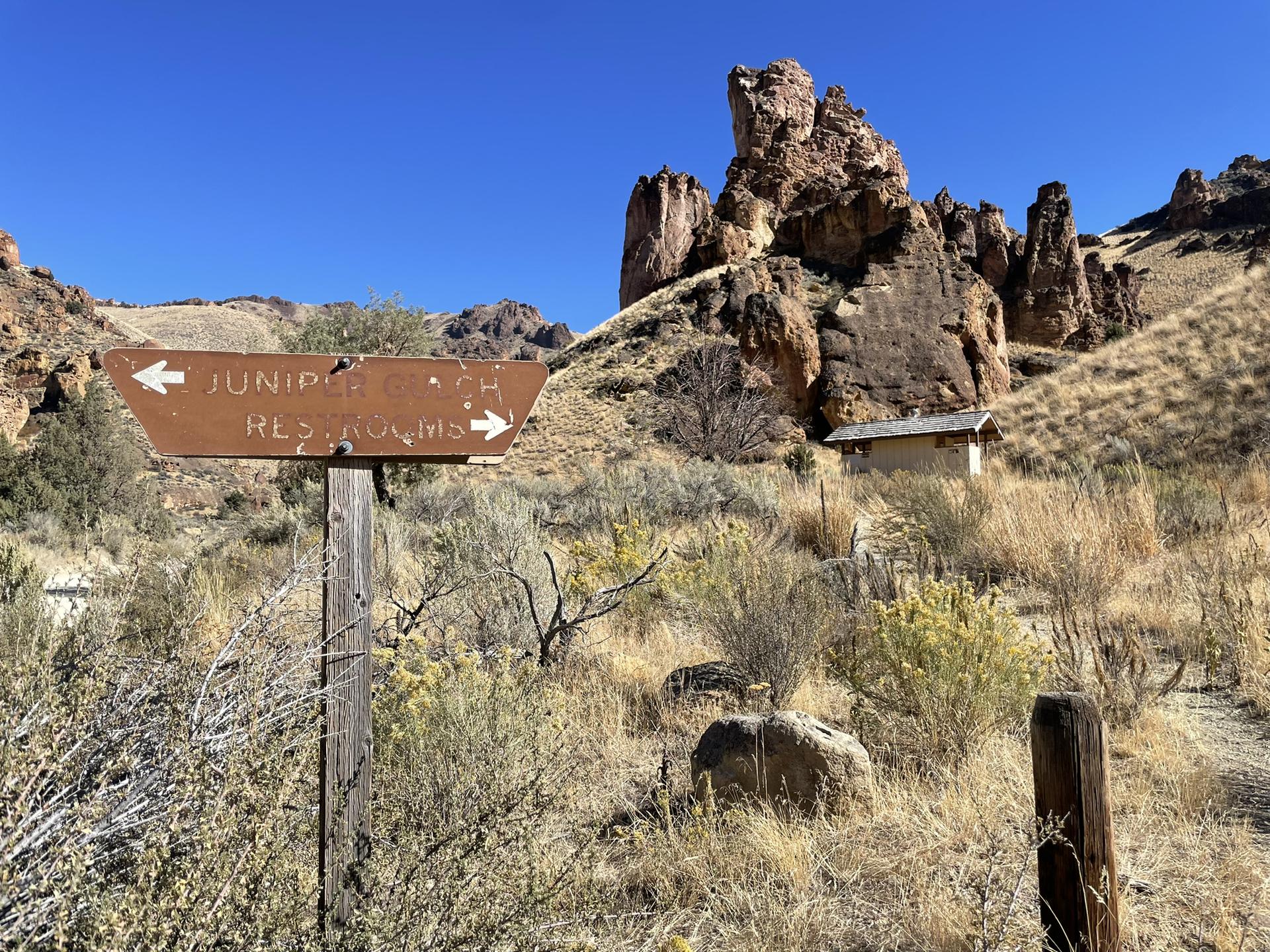 Brown trail sign pointing to restrooms in a desert landscape with rock formations.