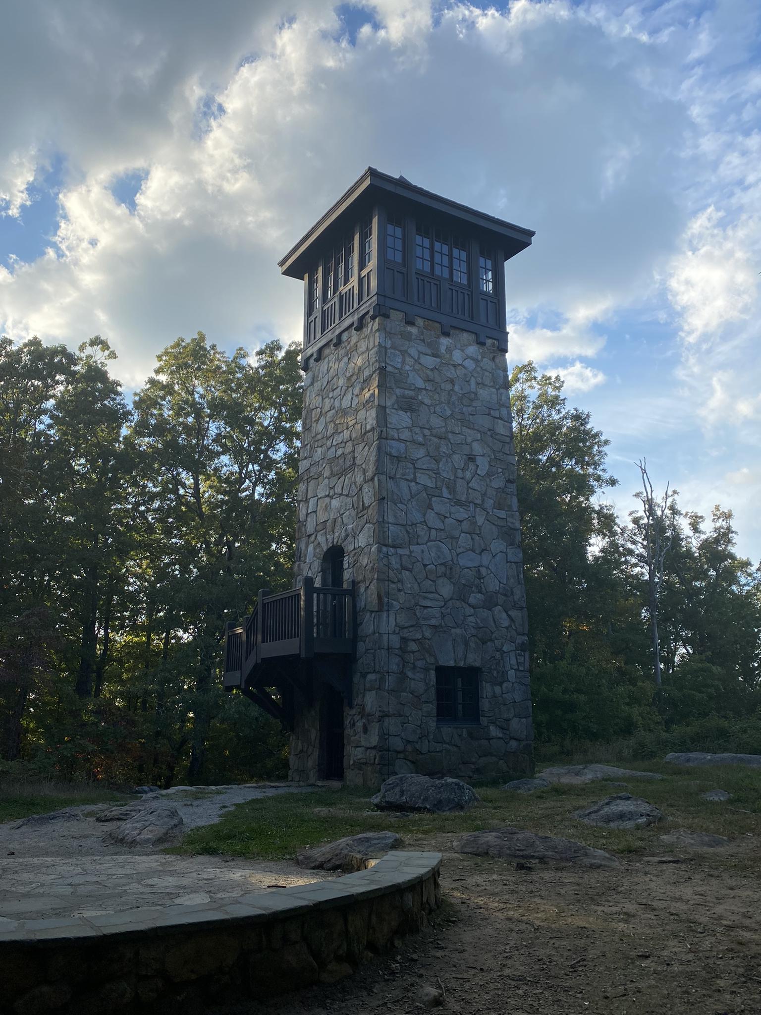Tall stone tower with a wooden top, surrounded by trees under a cloudy sky.