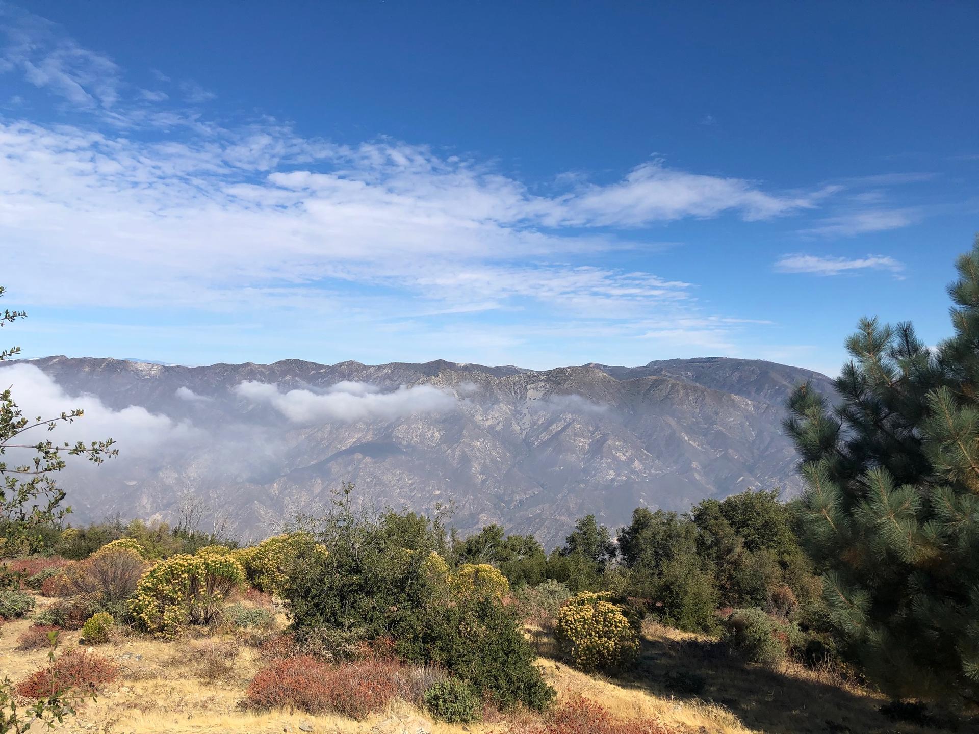 Mountain range partially obscured by low clouds under a blue sky.