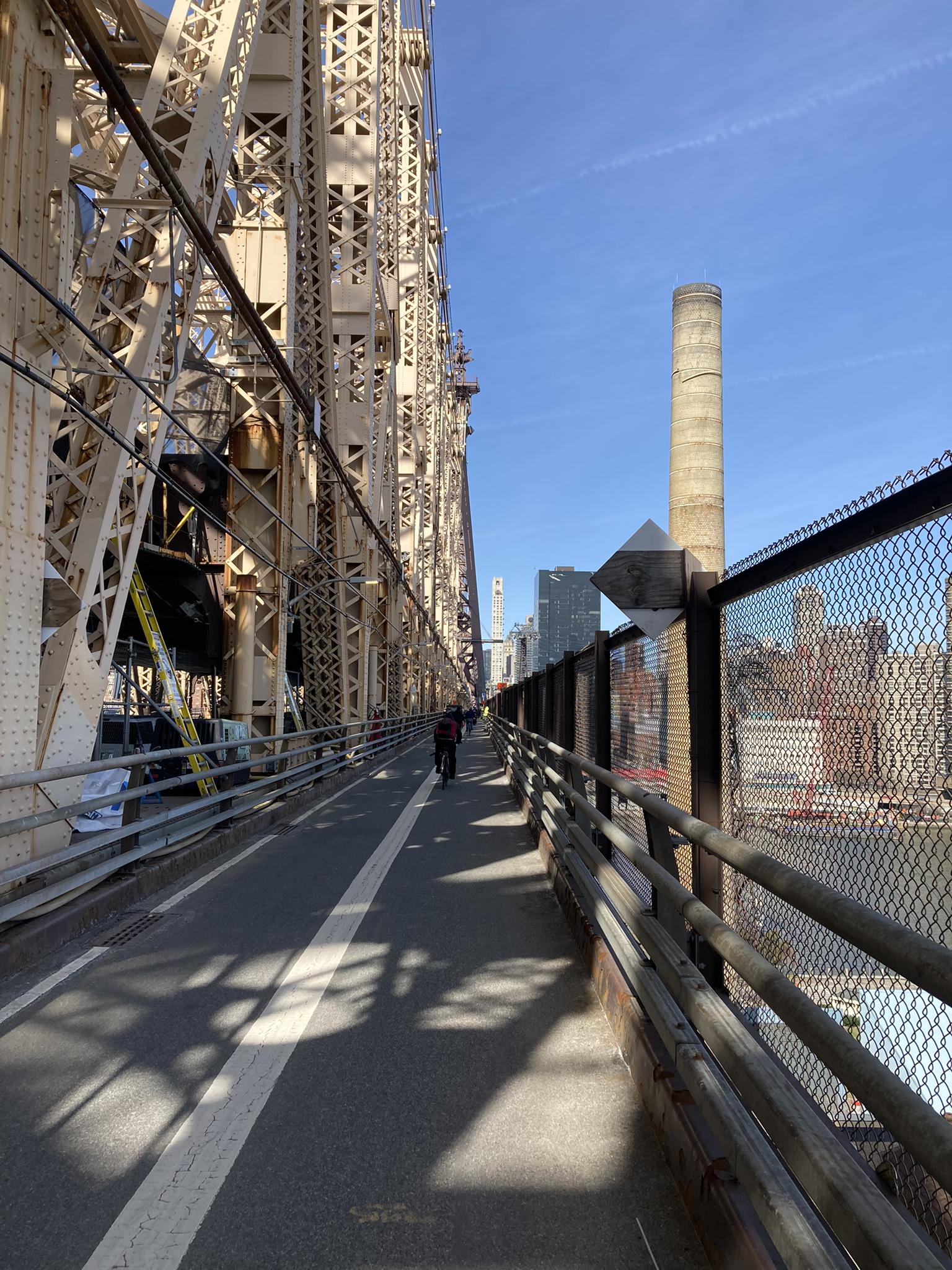 Pedestrian walkway on a large metal bridge with distant city views.
