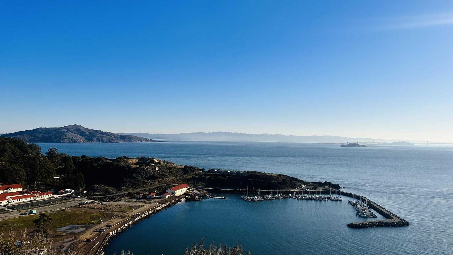 A marina filled with boats, distant mountains, under a clear blue sky.