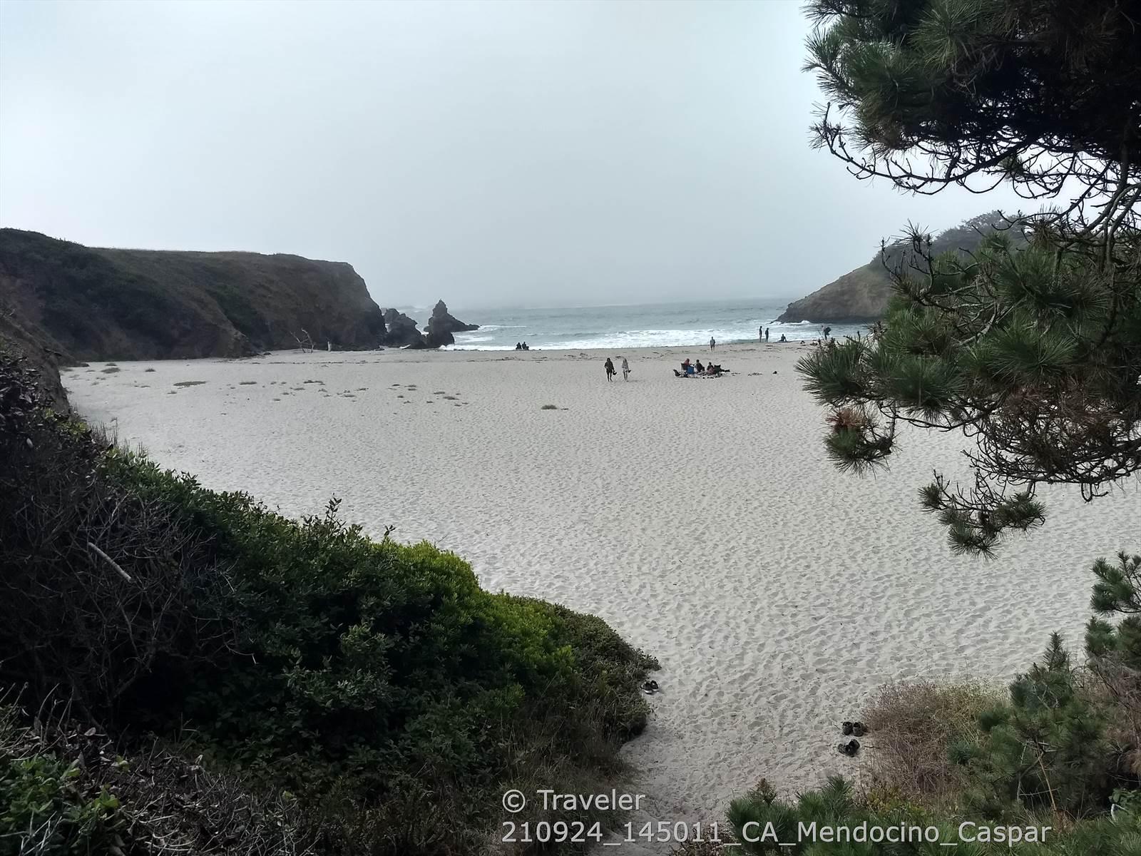 Overcast view of a wide sandy beach with distant ocean and people.