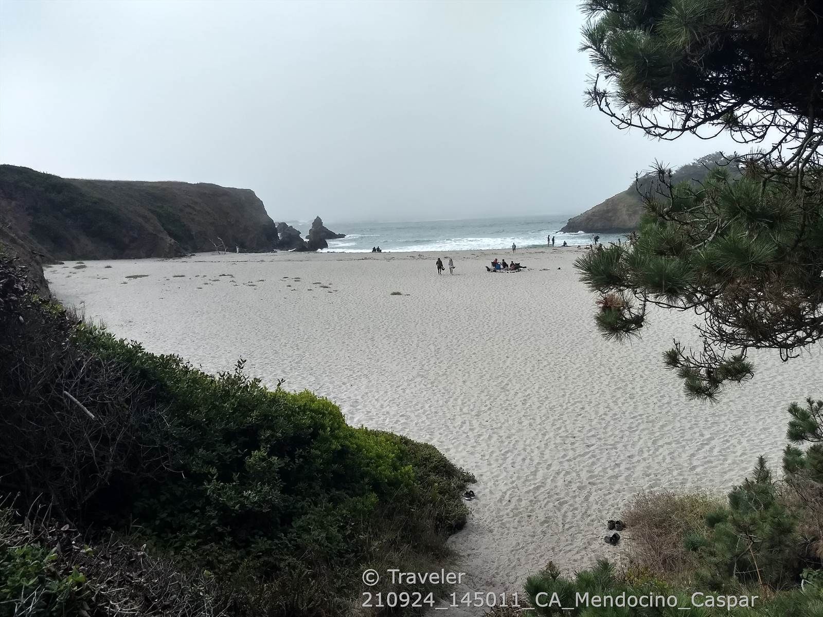 Overcast view of a wide sandy beach with distant ocean and people. - Ecological Staircase Trail