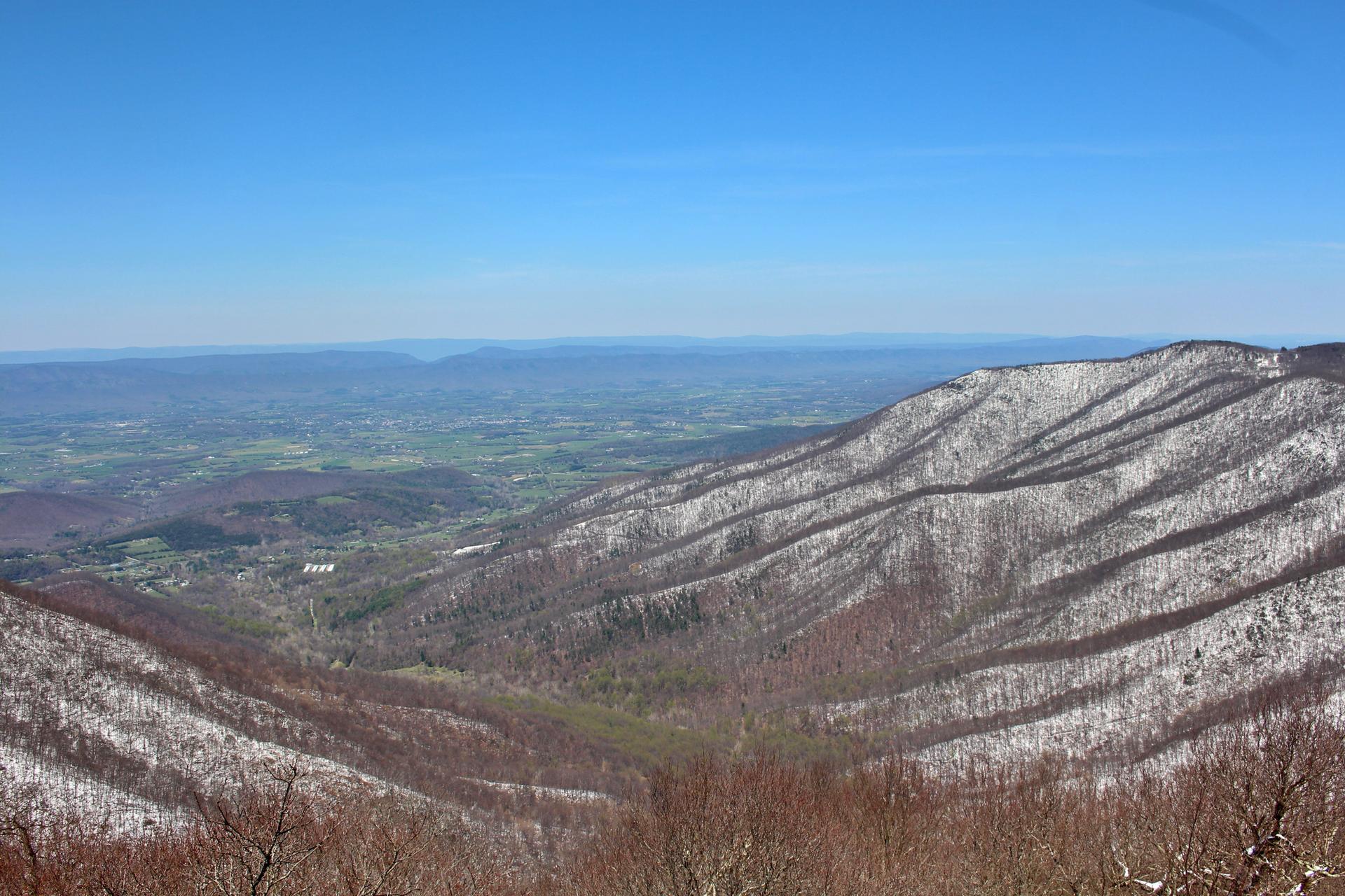 Snow-dusted mountains and a valley under a bright blue sky.