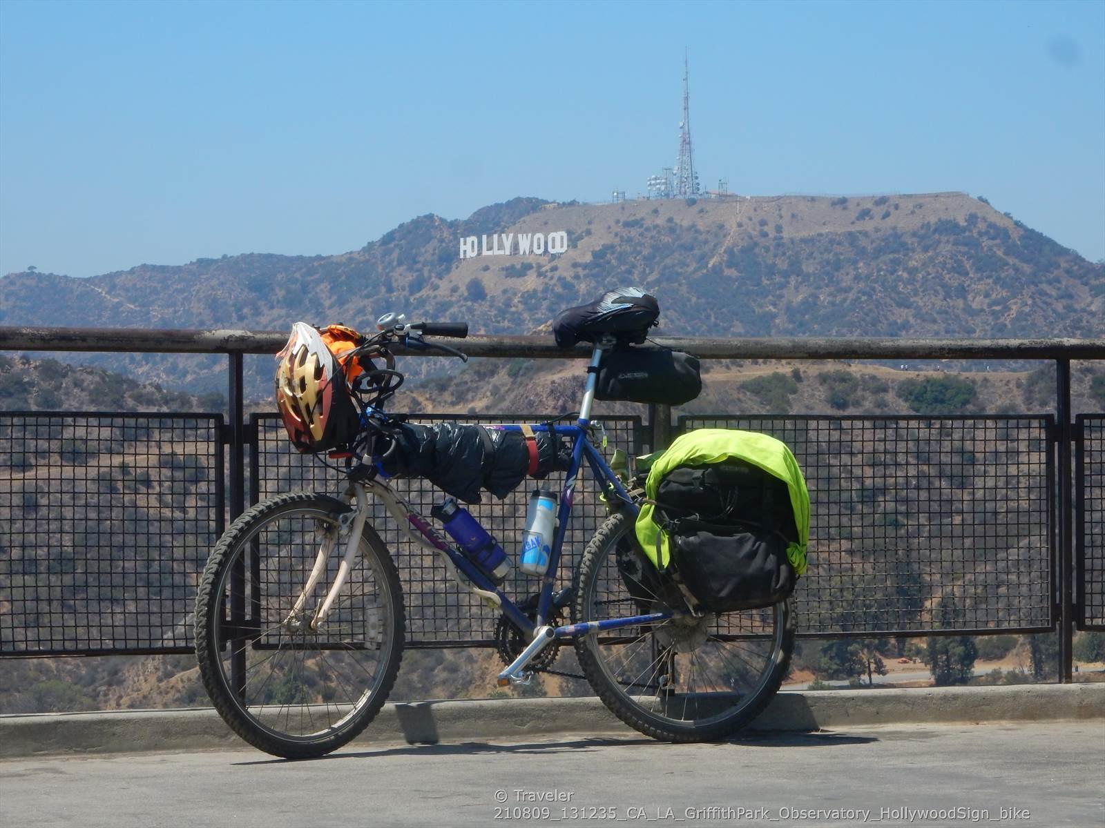 A touring bicycle with gear parked by a fence, hills in background.