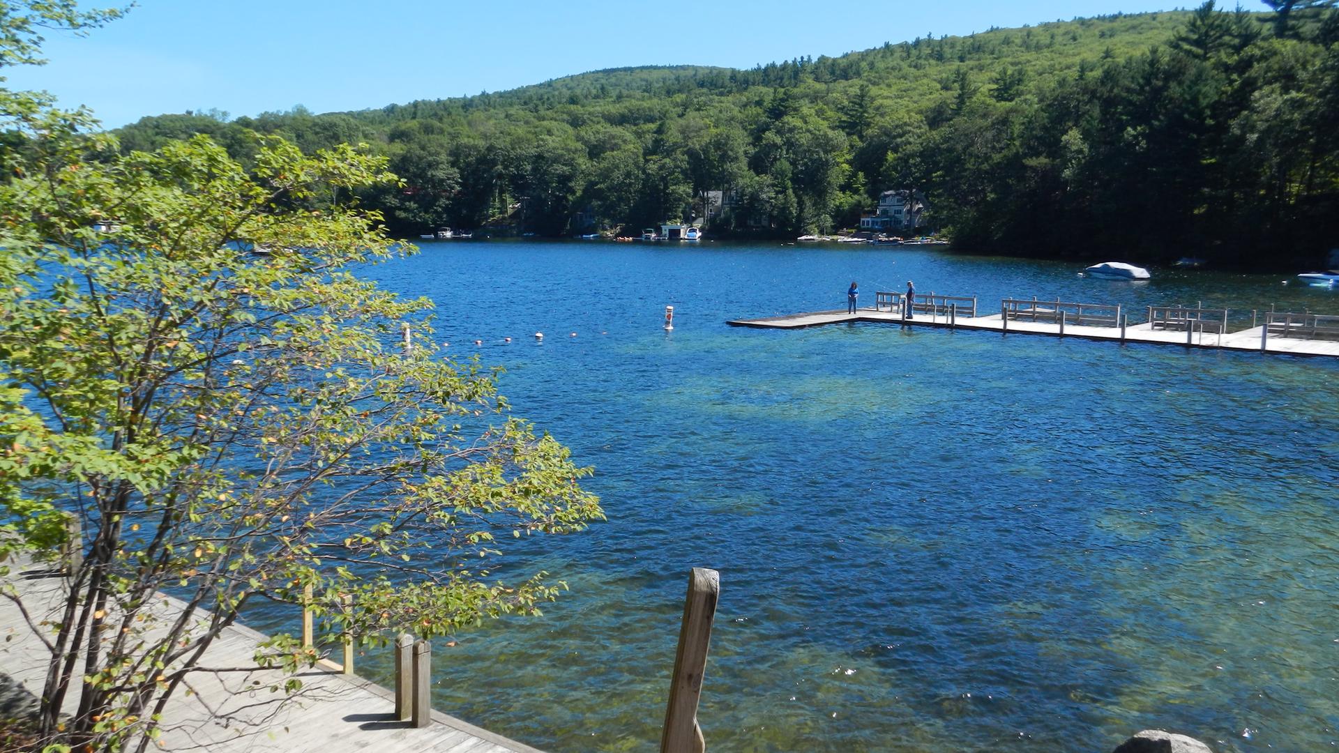 Bright blue lake with a long wooden dock and forested hills.