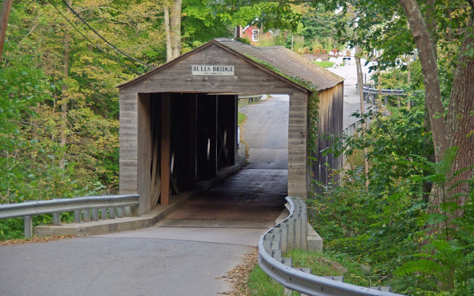 Rustic wooden covered bridge over a road, surrounded by green trees. - Bulls Bridge loop from Dover Plains