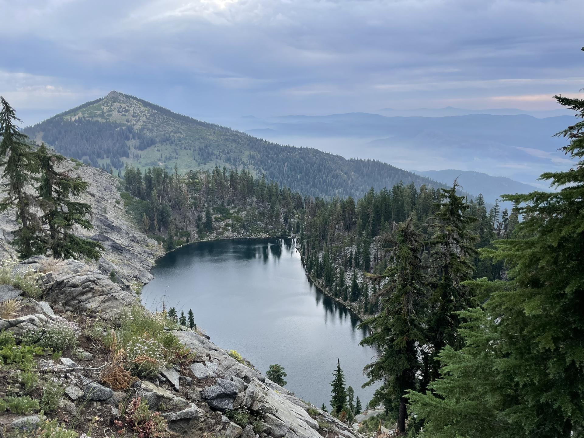 Lake nestled among forested mountains under a cloudy sky.