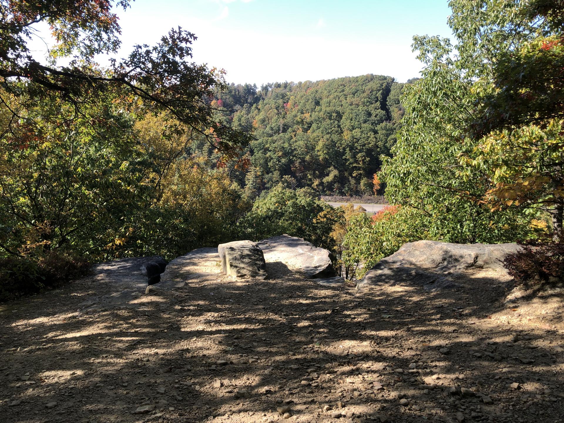 Rocky overlook with distant forested hills and a bright sky.