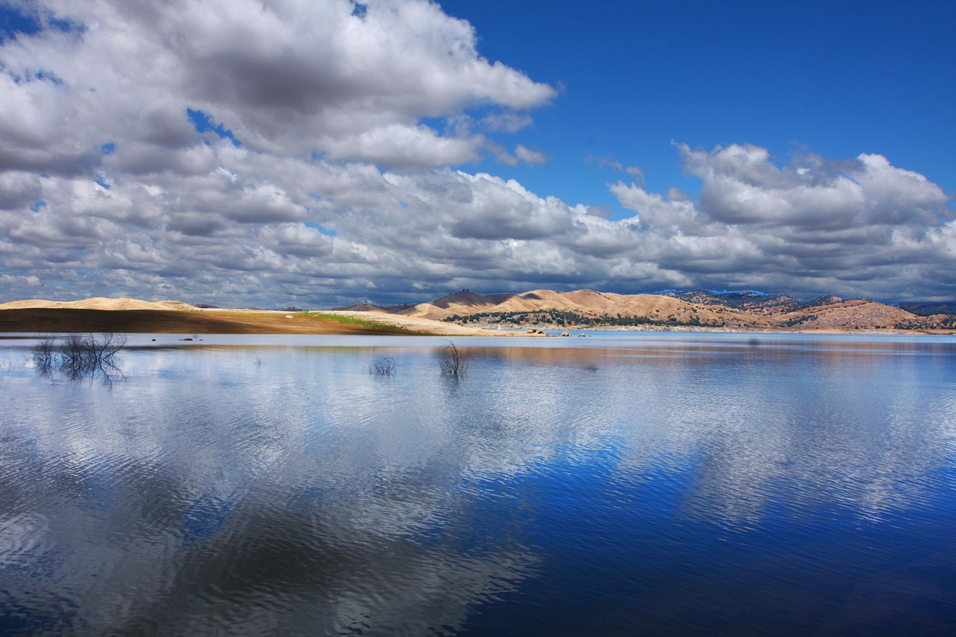Vast lake reflecting a partly cloudy sky, with dry hills in the background.
