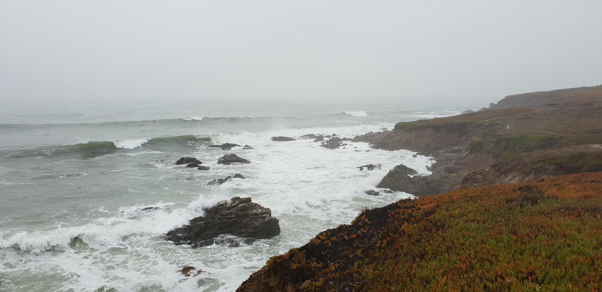 Overcast day with large waves crashing against a rocky, rugged coastline.
