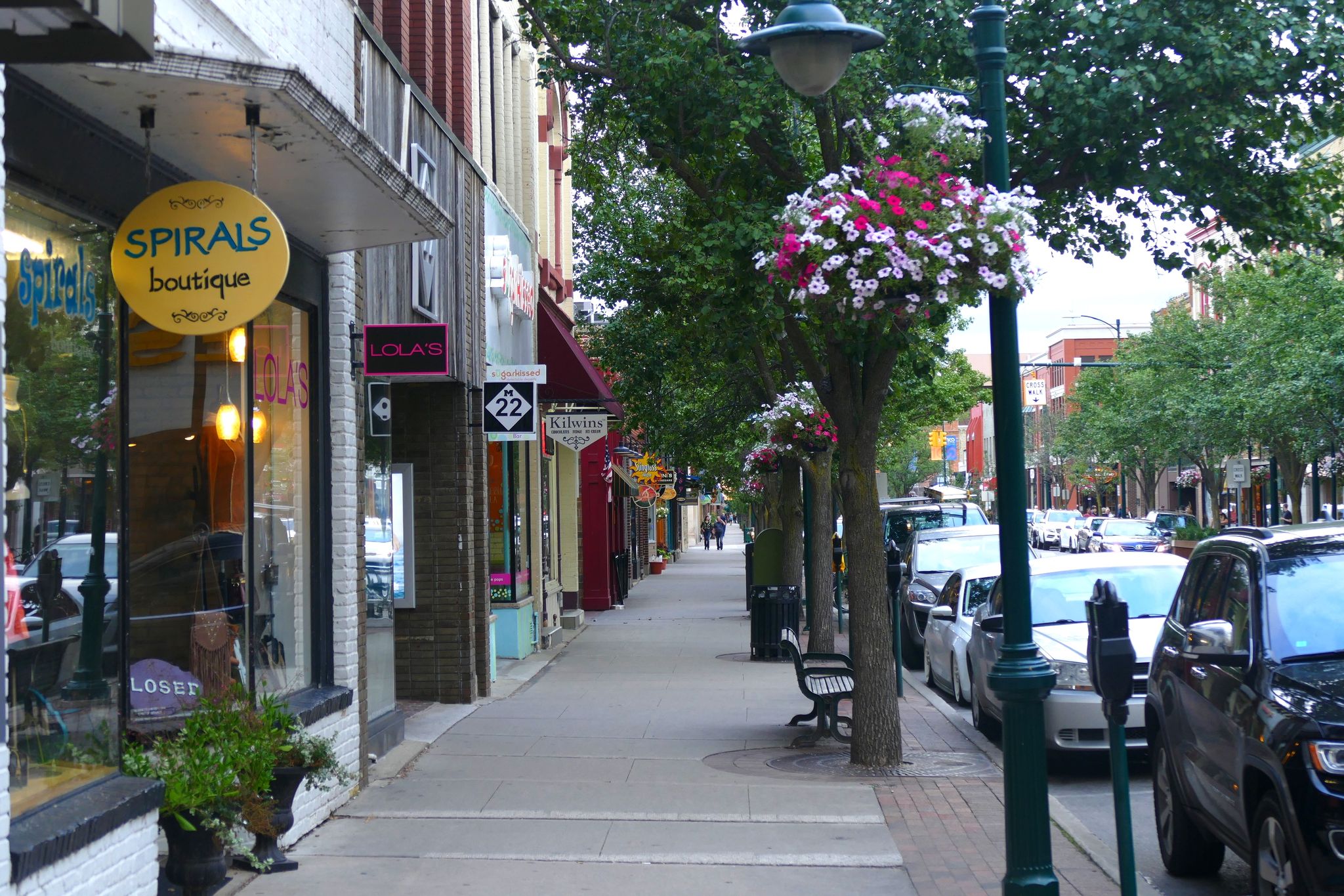 Sidewalk lined with shops, trees, and hanging flower baskets. - Traverse City – Boardman Lake Trail loop from Traverse City