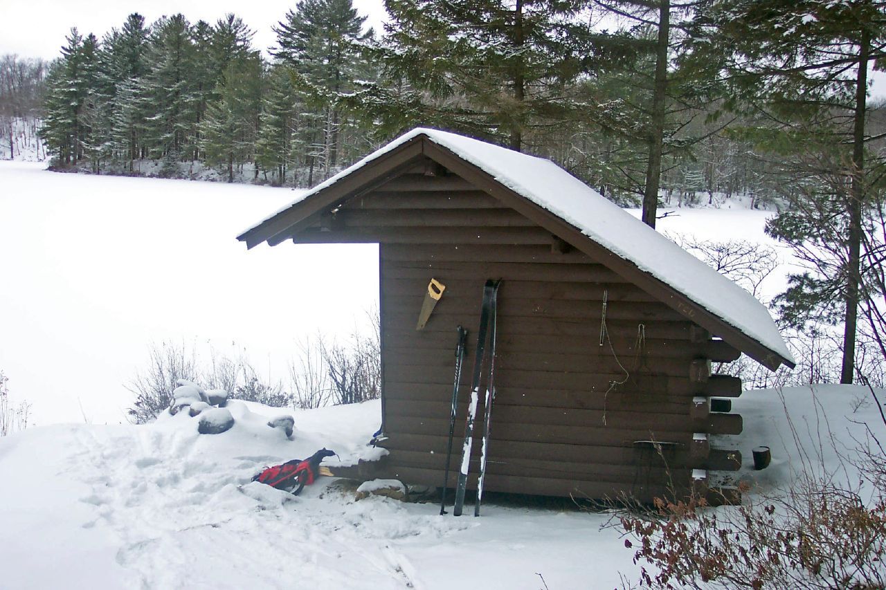 Snow-covered wooden cabin with skis, overlooking a frozen lake and pine forest. - Middle Settlement & Middle Branch Lakes loop