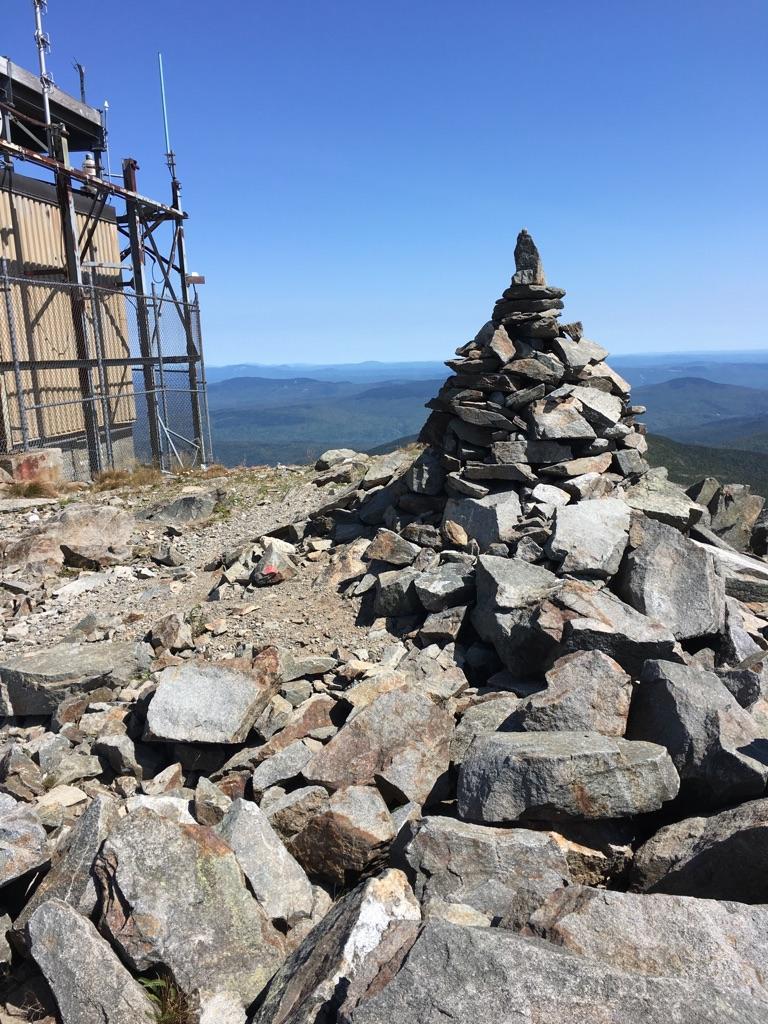 A large stone cairn on a rocky mountain summit under clear blue sky.