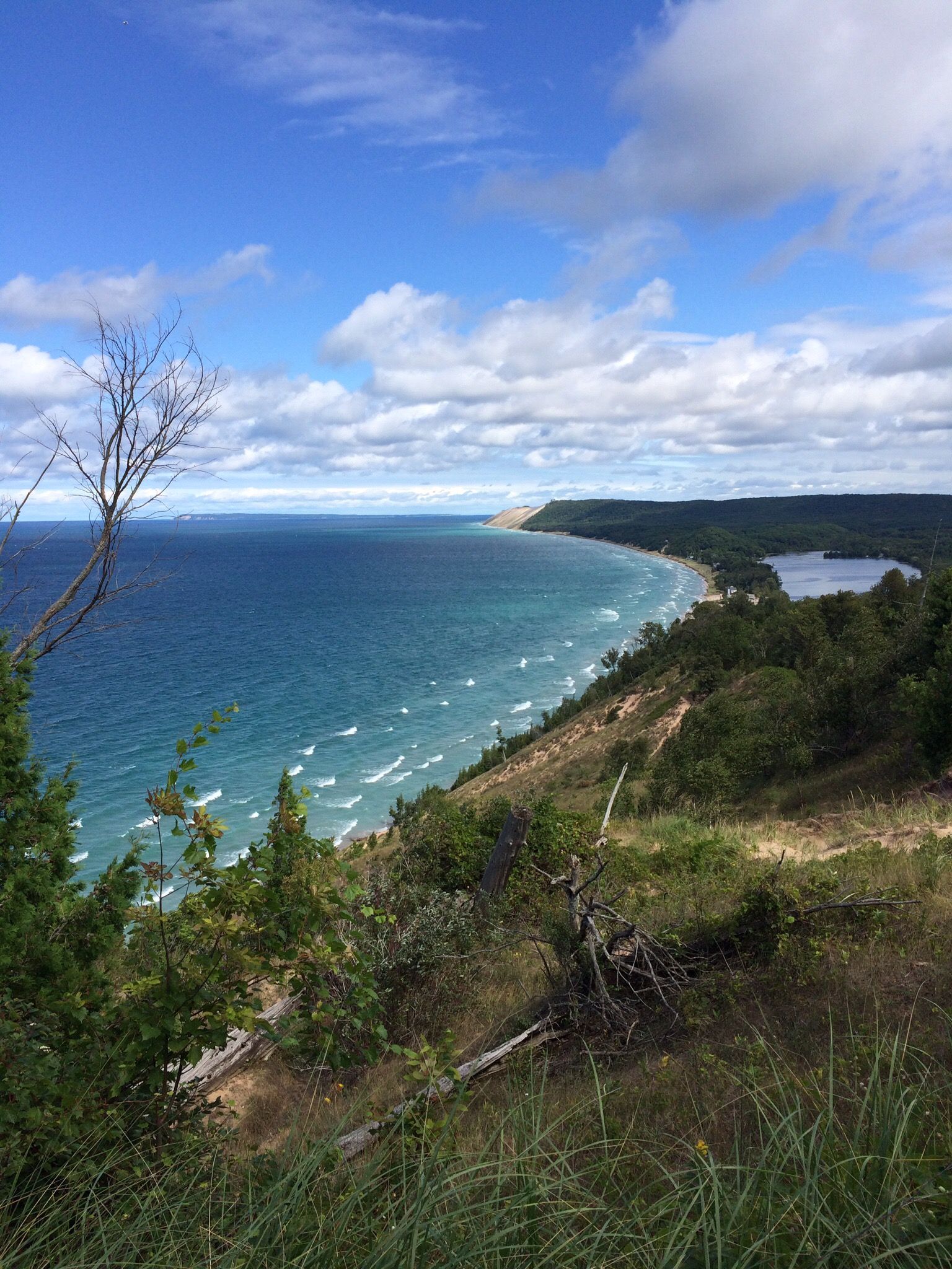 Wide view of blue water, sandy coastline, and green hills under a cloudy sky. - Empire Bluff Trail