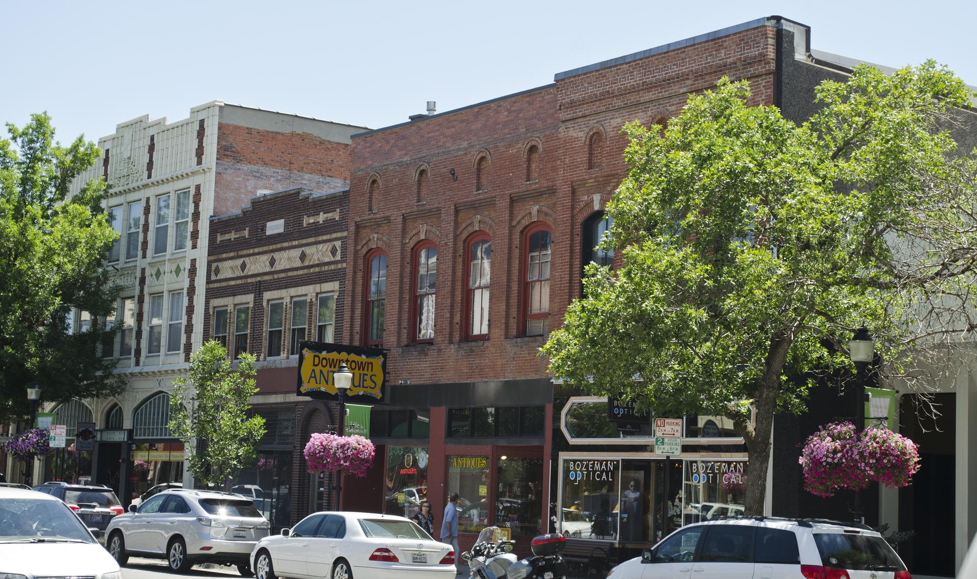 Sunny street scene with historic brick buildings, trees, and parked cars.