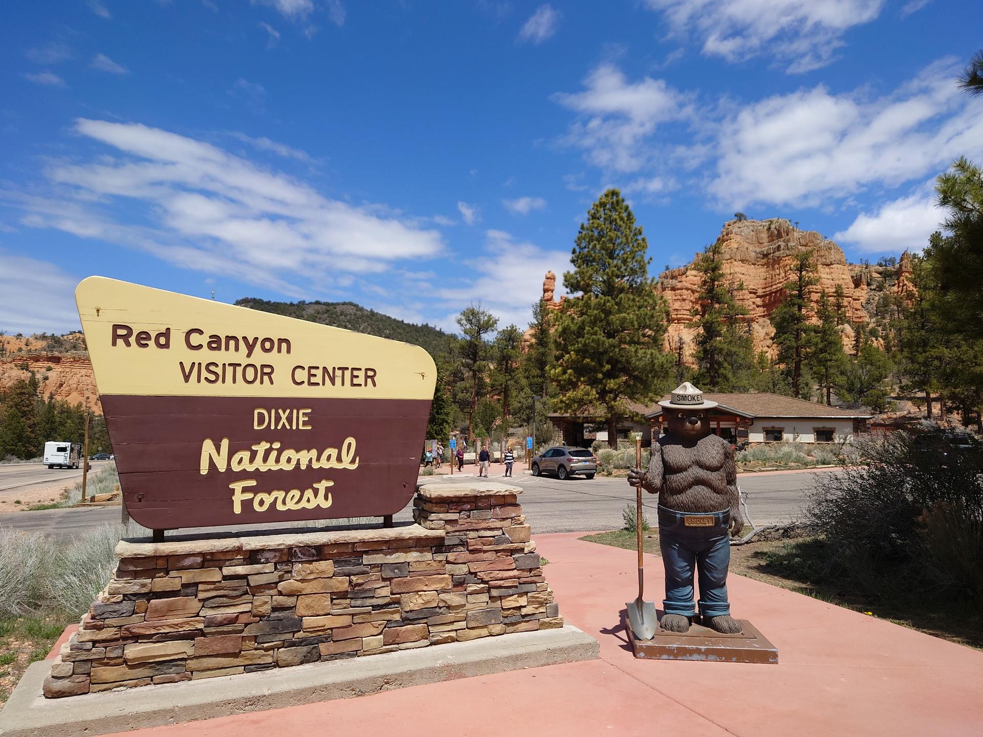 A visitor center sign and Smokey Bear statue under a bright blue sky.