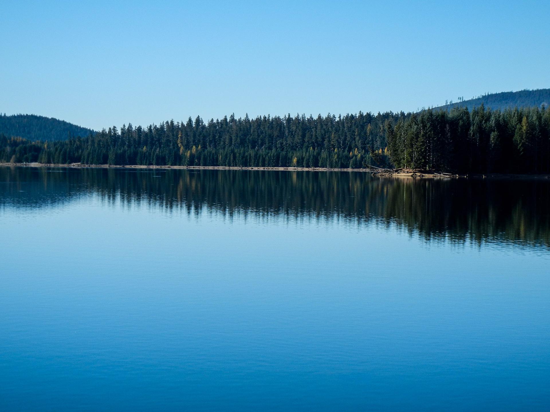 A calm blue lake reflects distant forested hills under a clear sky.