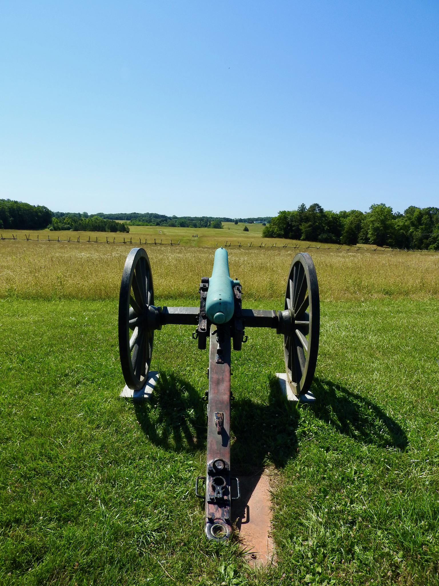 An antique cannon points across a bright, sunlit green field.