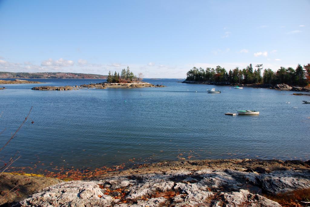 Sunny view of a rocky coastline with boats on blue water and forested islands.