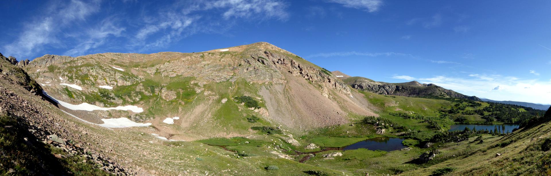 Panoramic view of vast, green mountain landscape with small lakes under a blue sky.