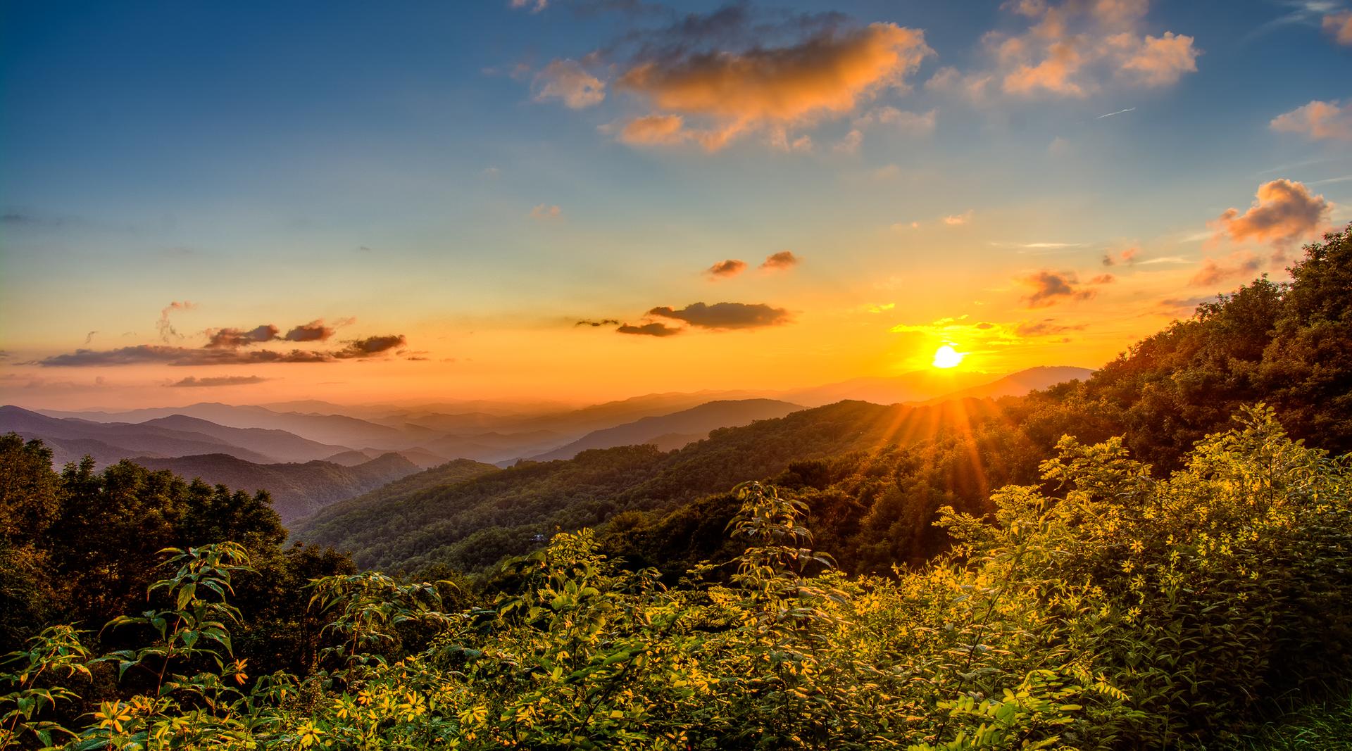Golden sunset over lush green mountains with sun rays piercing through.