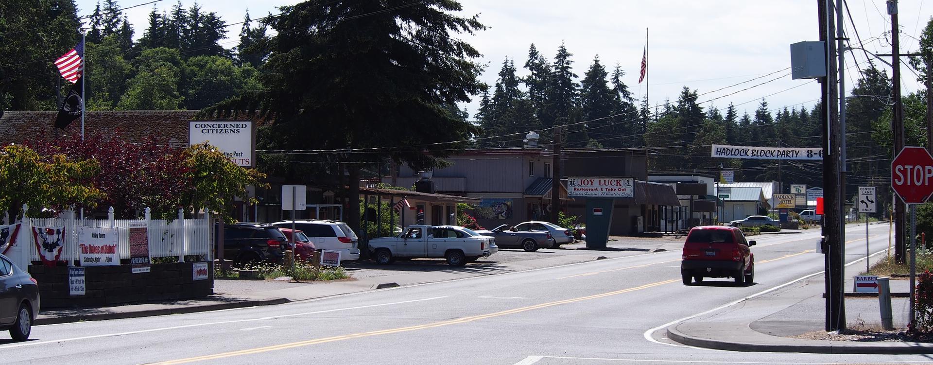 A sunny street scene with buildings, parked cars, and a red car driving.