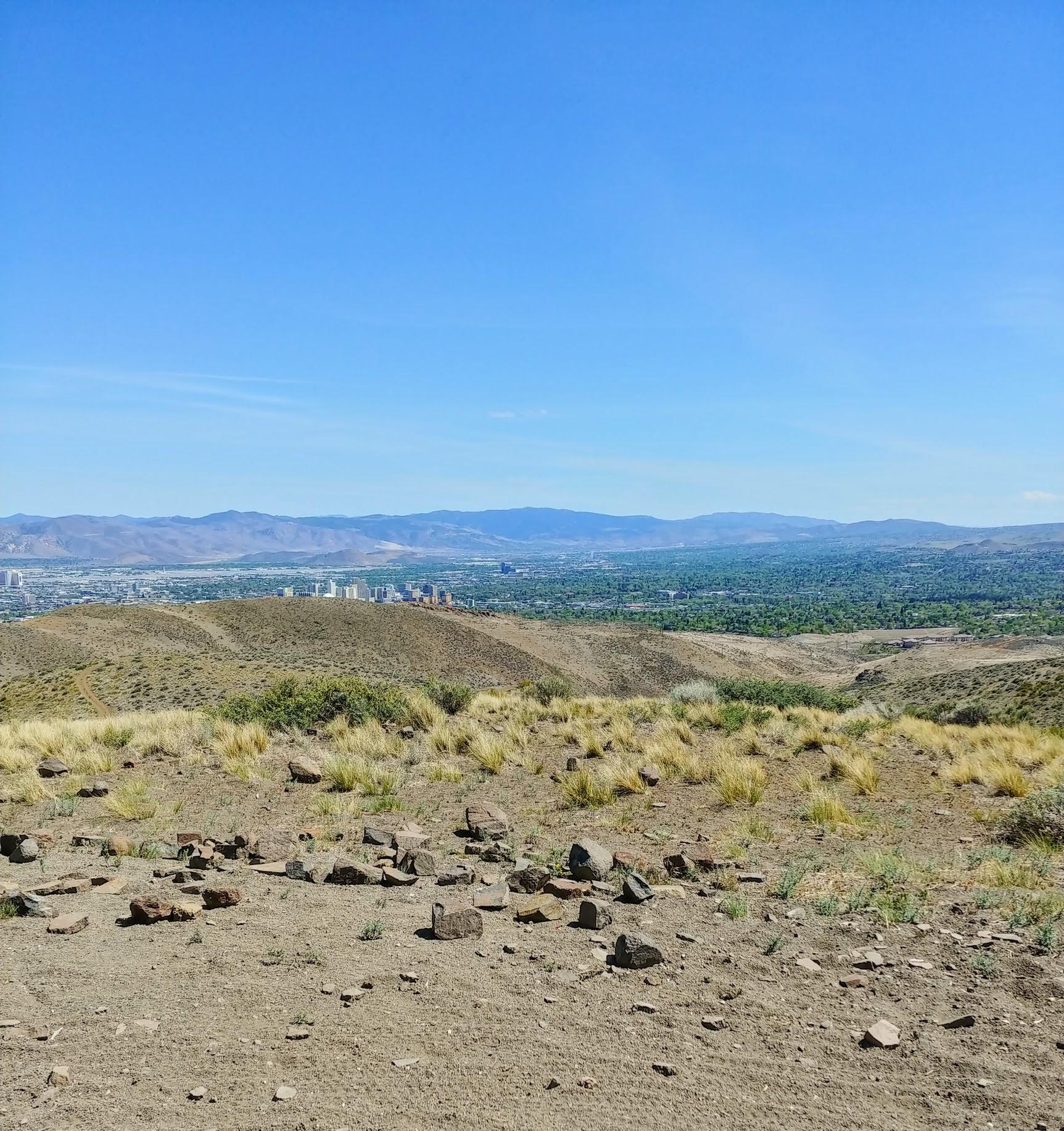 Expansive desert hills under clear sky, with a distant city and mountains.