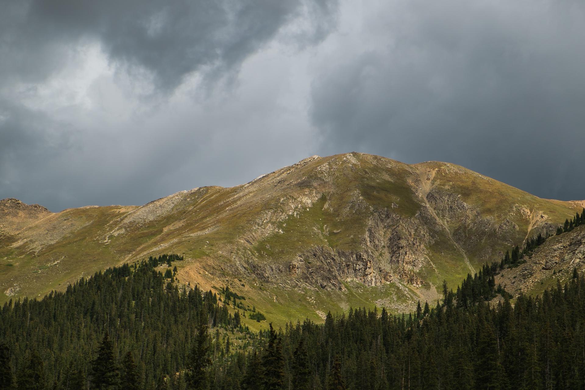 A forested mountain stands under dramatic, dark storm clouds.