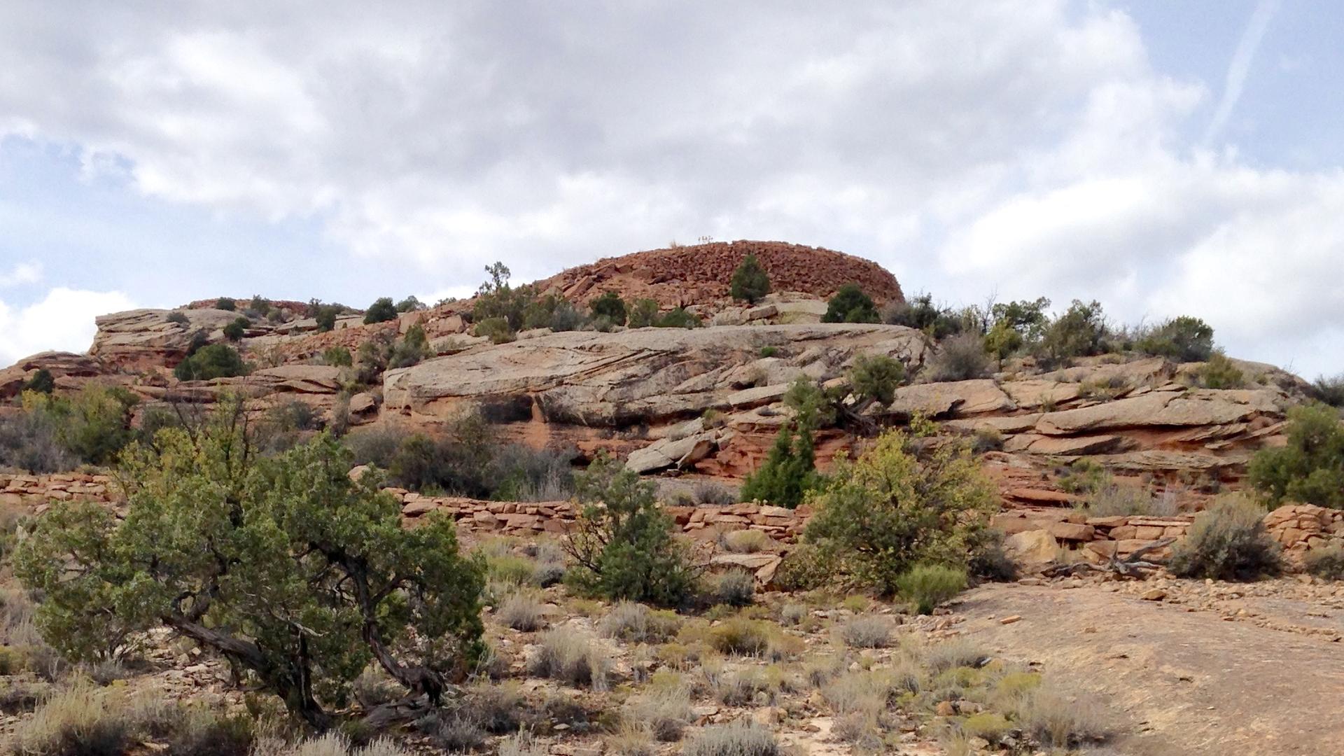 Rocky desert hill covered in sparse bushes under a cloudy sky.