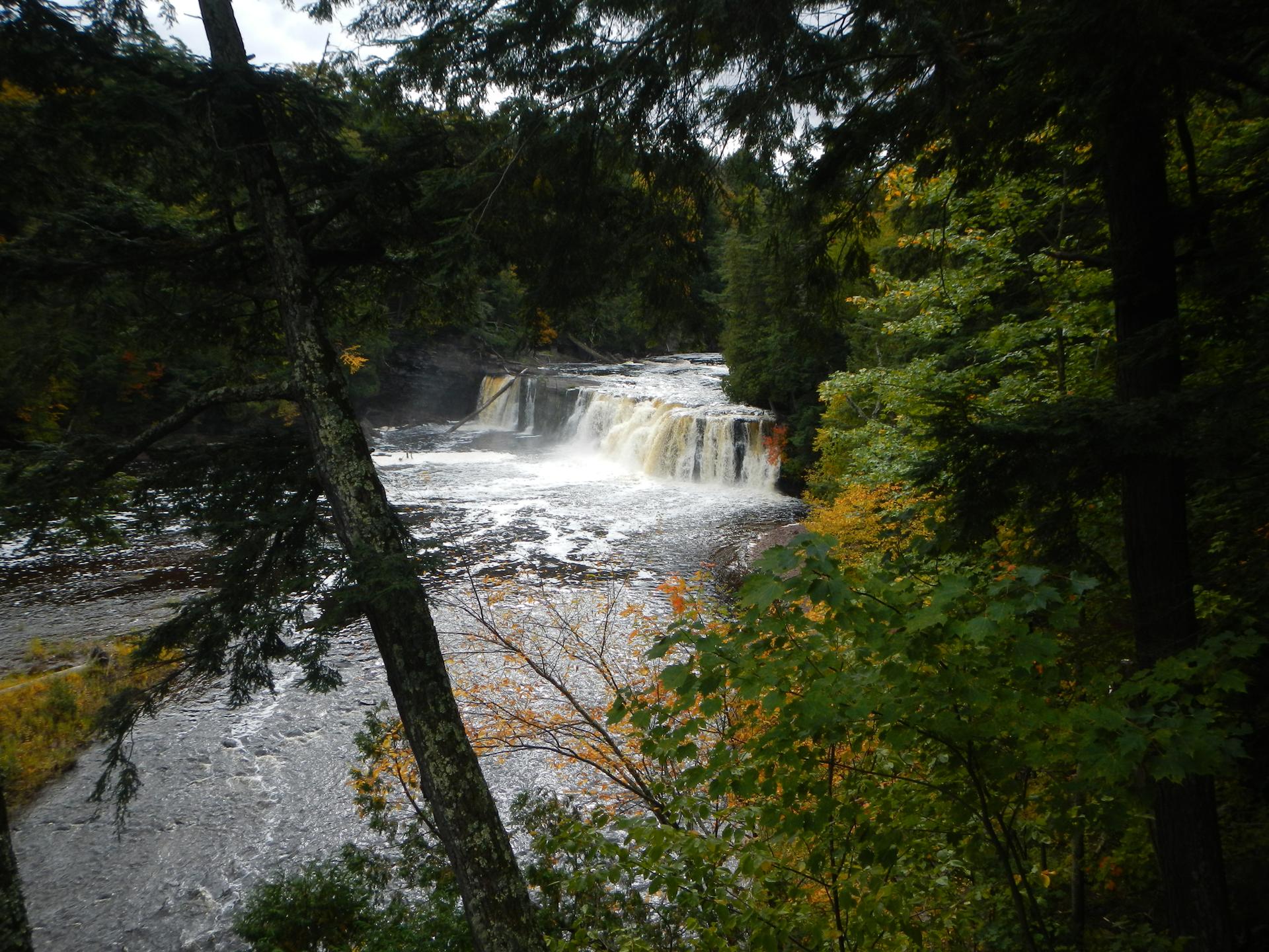 Wide waterfall flows over a rocky ledge, framed by dark forest.