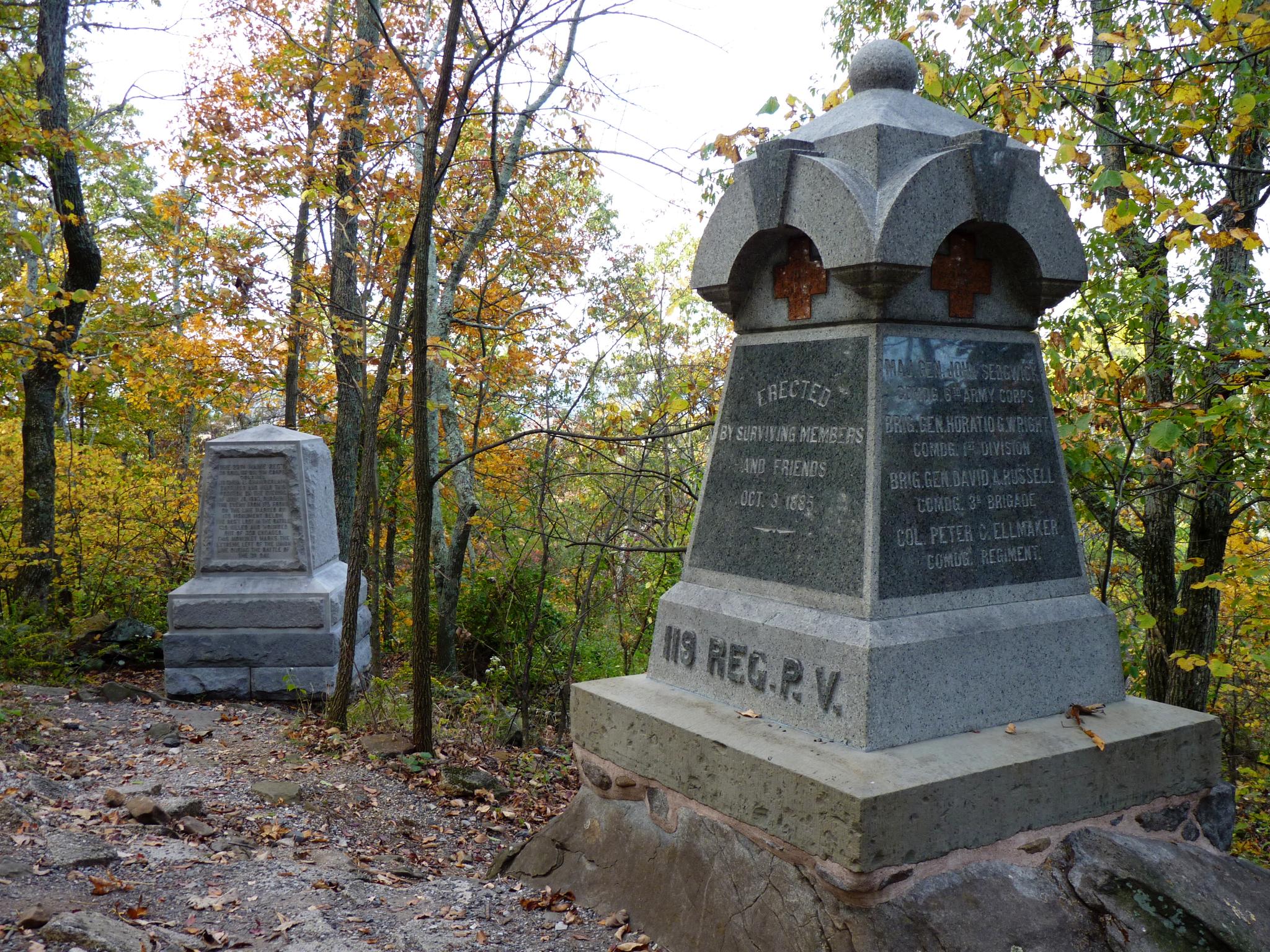Two stone monuments stand in an autumn forest under diffused light.