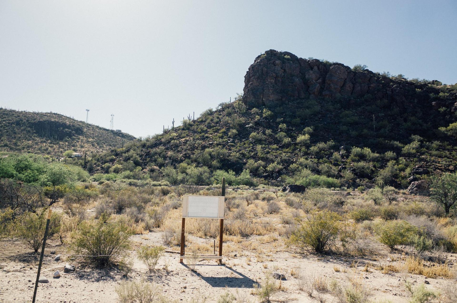 Arid desert landscape with a blank sign in the foreground and rocky hills.