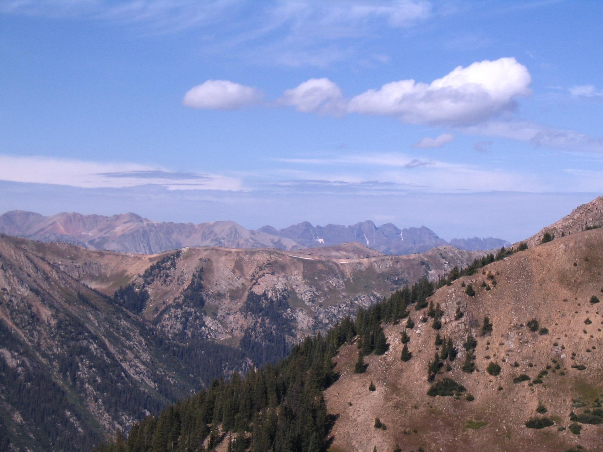 Expansive mountain range under a bright blue sky with scattered clouds.