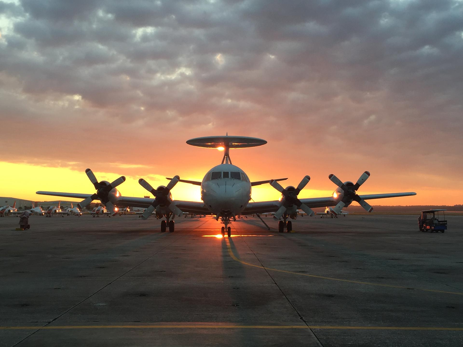 Large propeller airplane on tarmac silhouetted against a vibrant sunset sky.