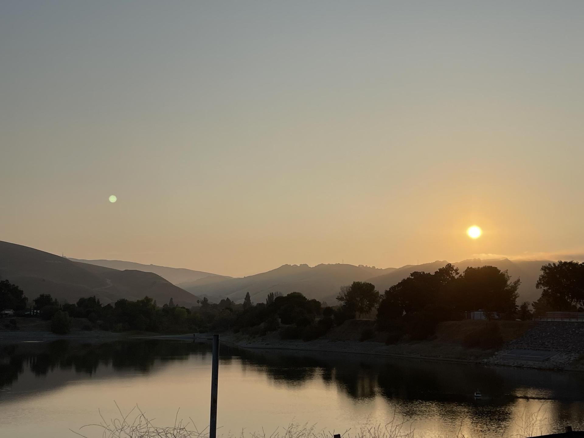 Wide view of a golden sunset over a tranquil lake and distant mountains.
