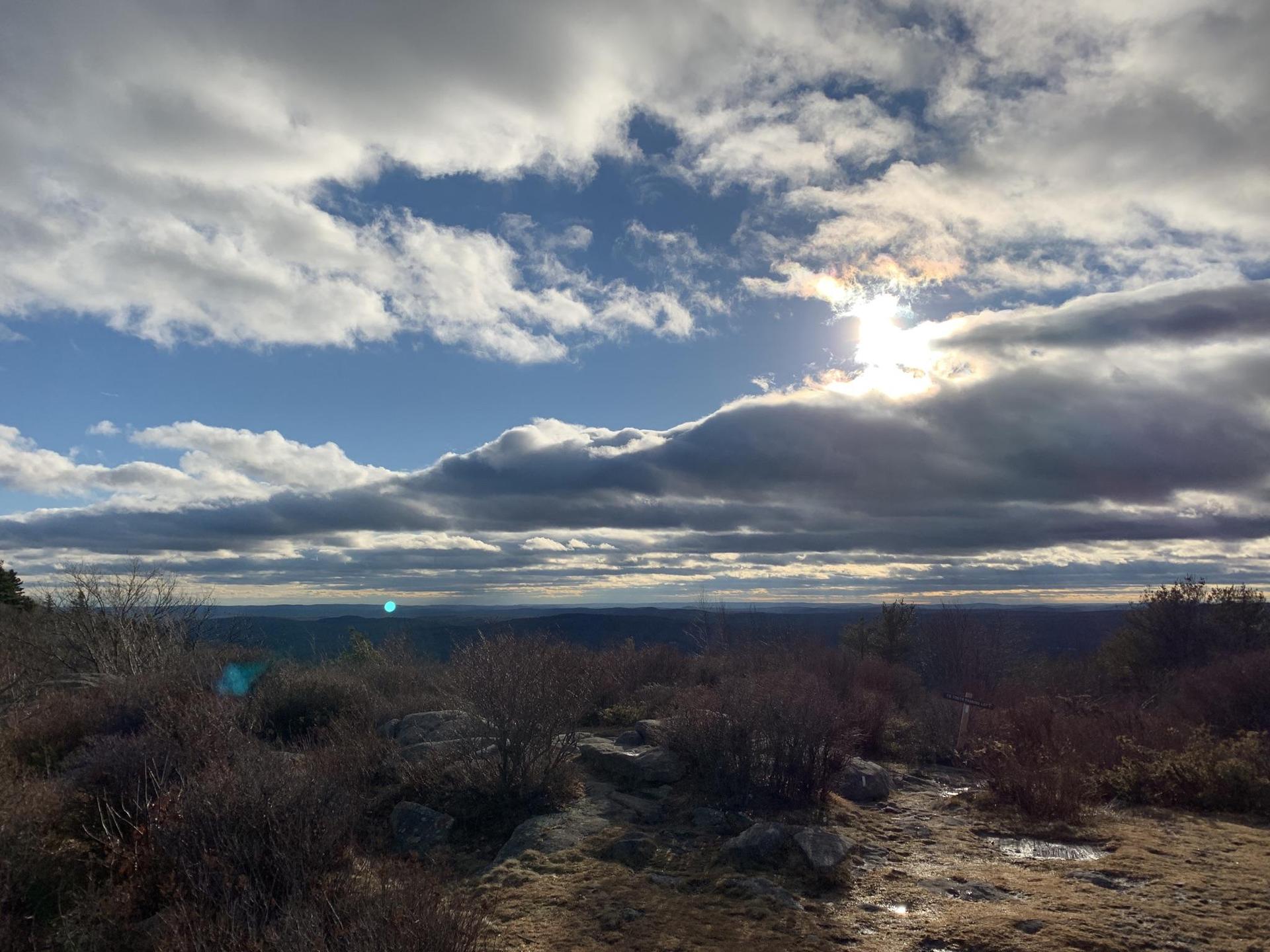 Expansive landscape with sun breaking through dramatic clouds over a distant horizon.
