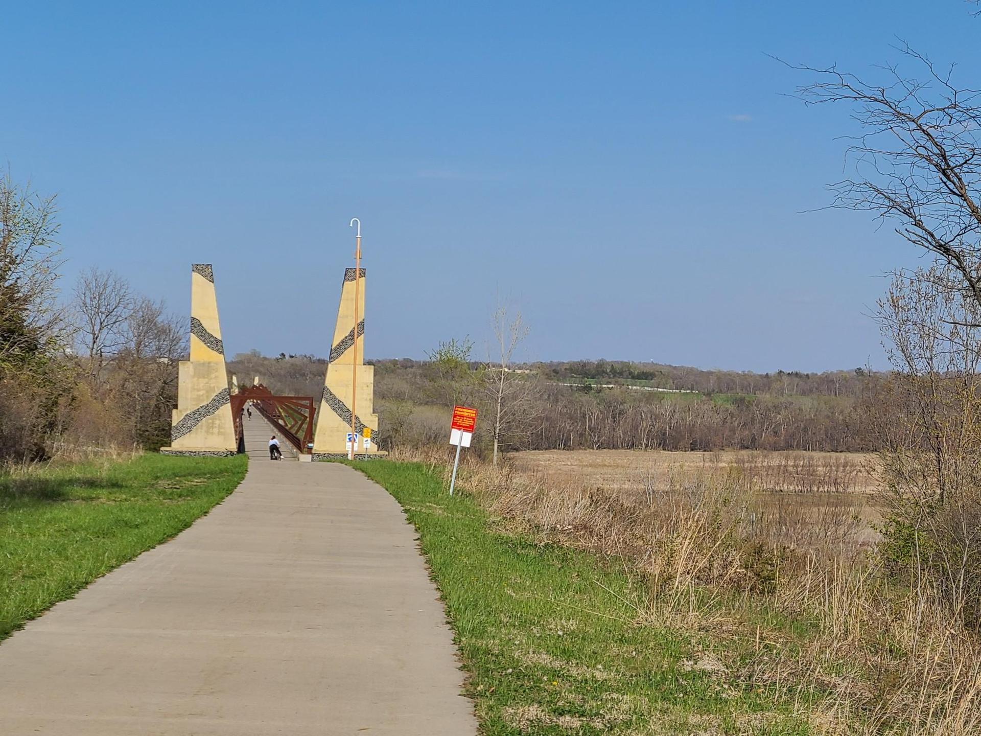 Paved path leading to tall, artistic gateway structures under a clear blue sky.