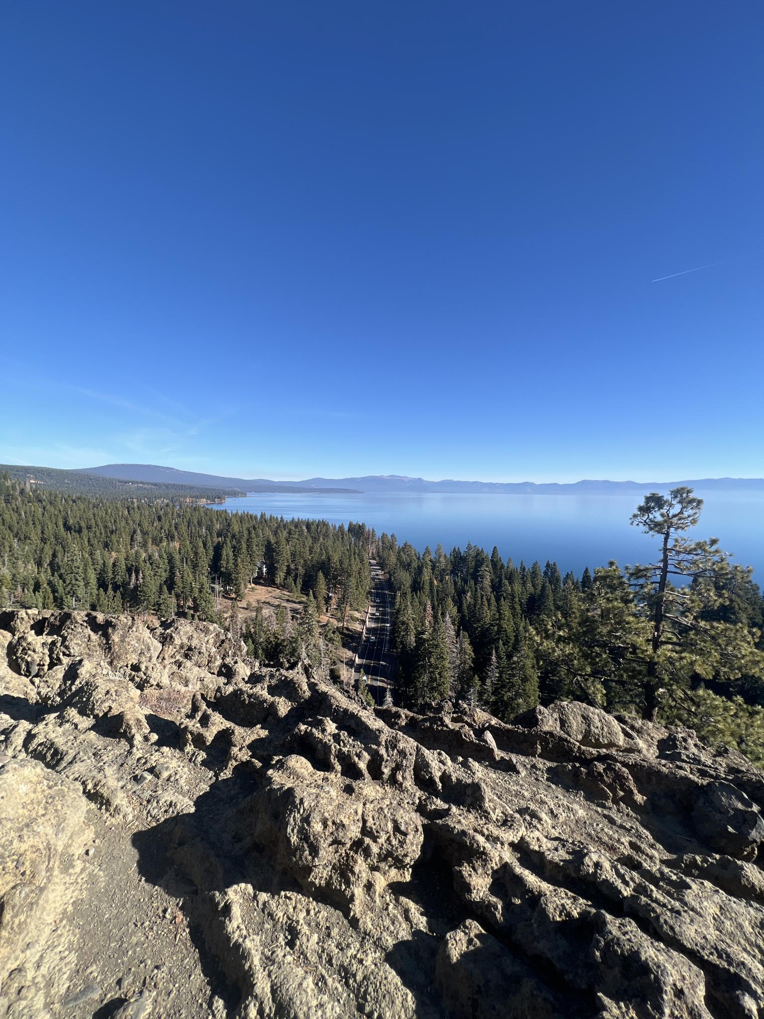 Vast blue lake and green forest viewed from a rocky mountain overlook.
