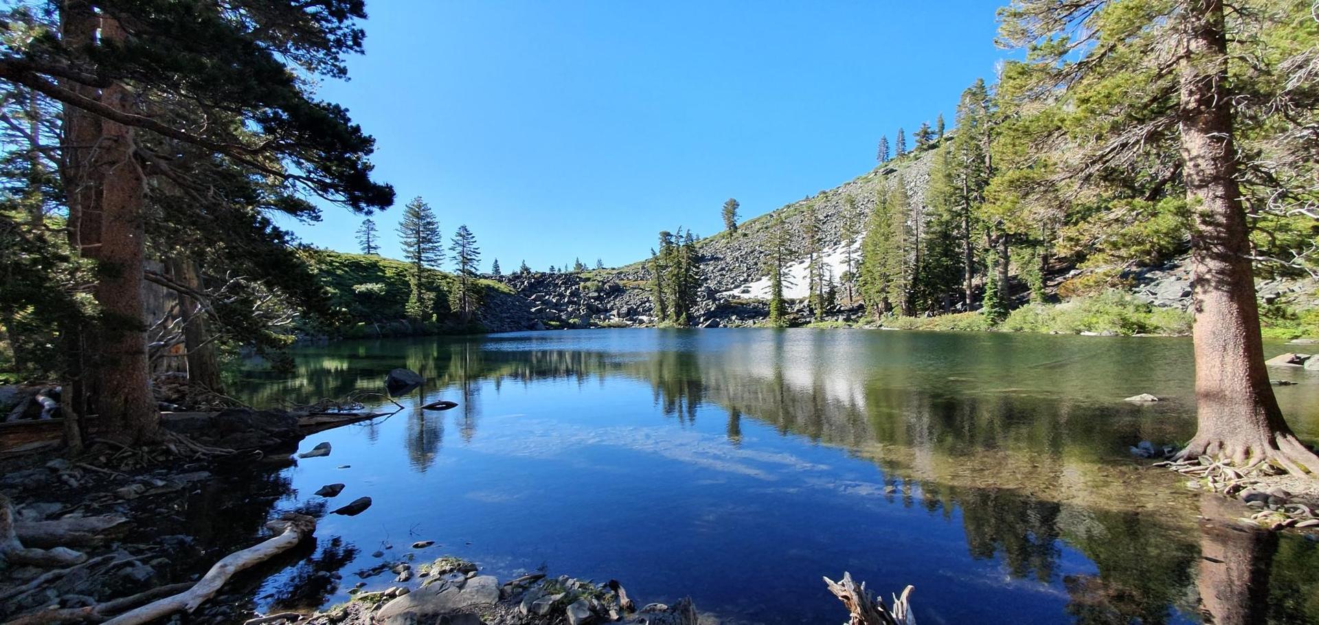 Serene blue lake surrounded by tall pine trees and rocky, snow-dusted slopes.