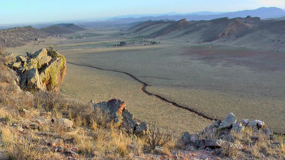 Vast dry valley with a winding path, seen from a rocky, sunlit hillside. - Coyote Ridge Trail