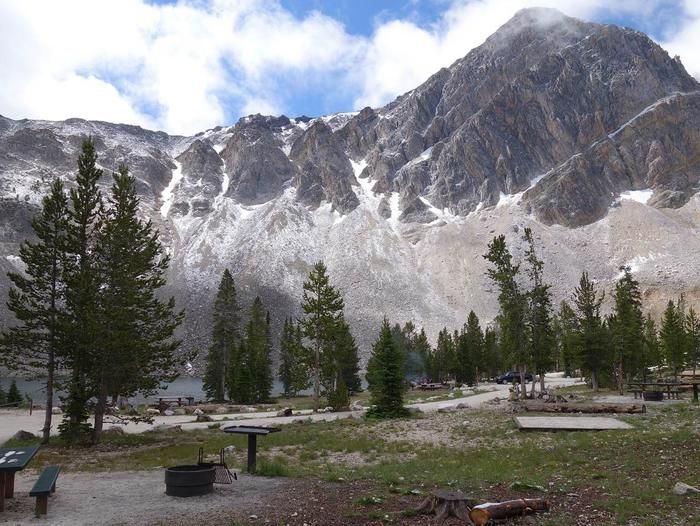 Campsite with pine trees, a lake, and snow-dusted mountains under a bright sky. - Meadow Lake Trail